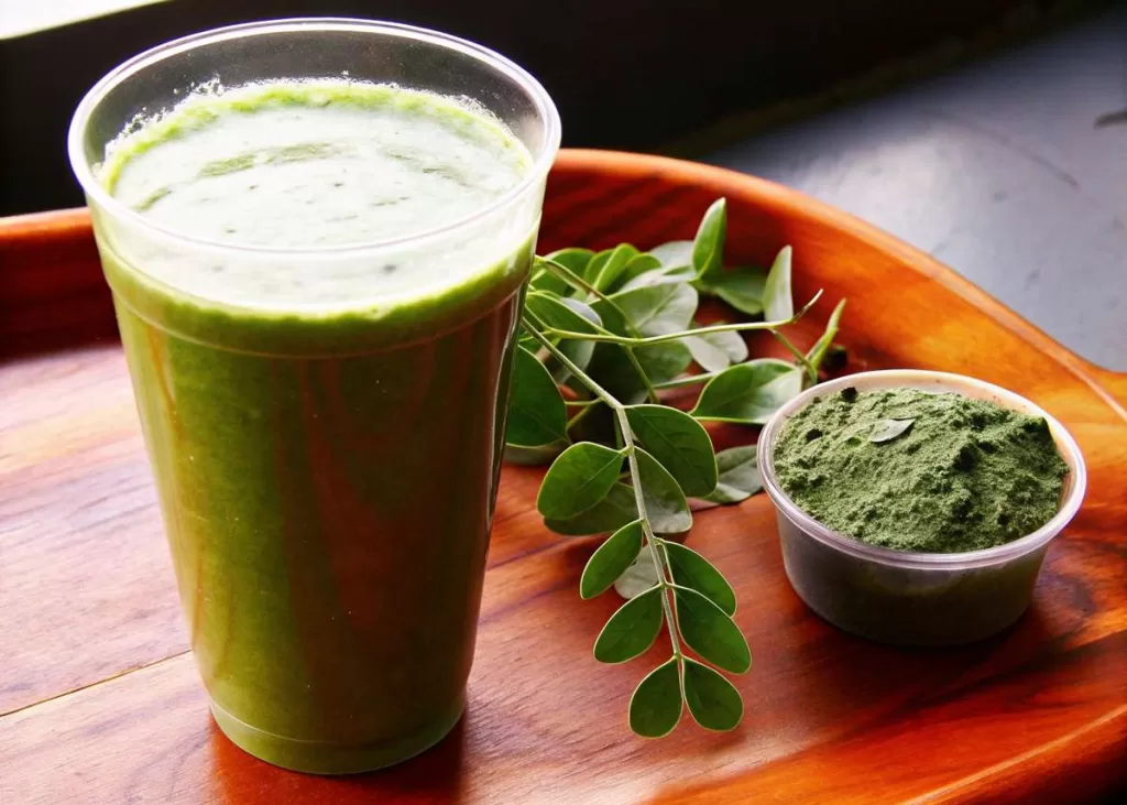 Smoothie verde com pó de moringa e folhas frescas decorativas.